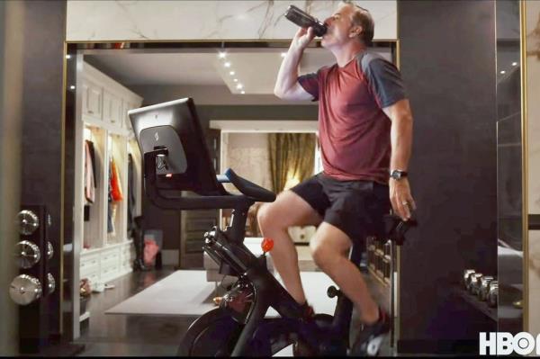 A man on a stationary Peloton bike drinking from a bottle - Scene from Sex and the City