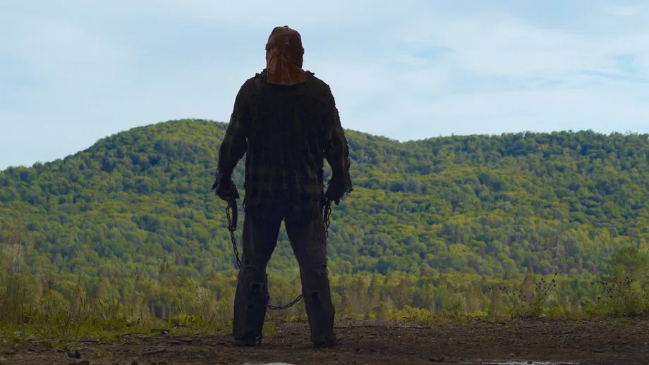 Ry Barrett as Johnny in In A Violent Nature holding a chain while looking at the horizon in a forest